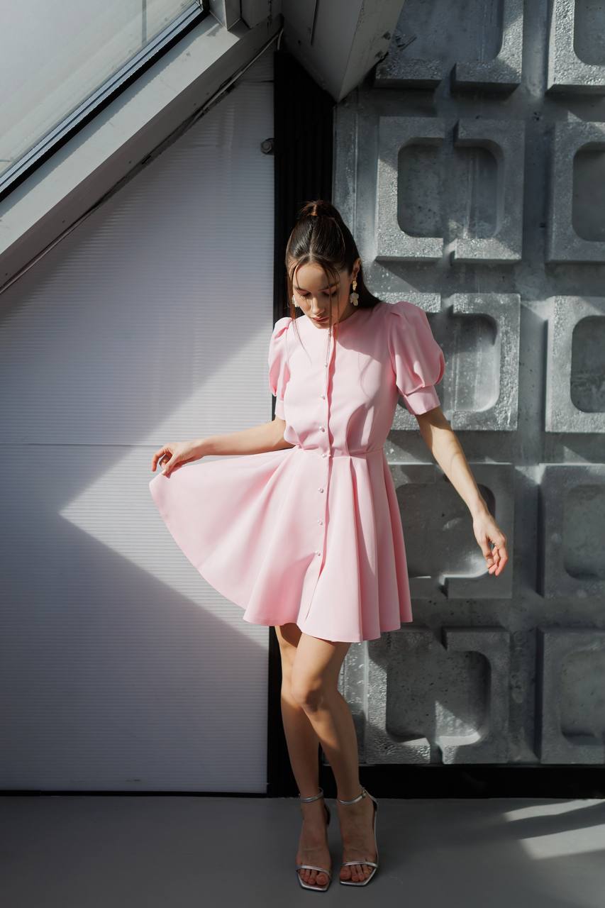Woman in a pink dress standing against a textured wall.