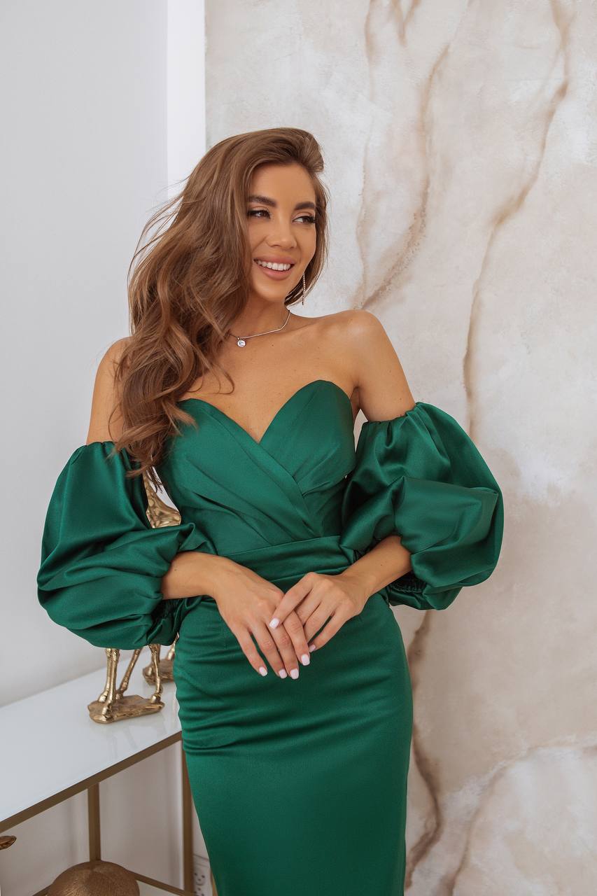 Woman wearing a green dress with puffed sleeves against a marble wall.