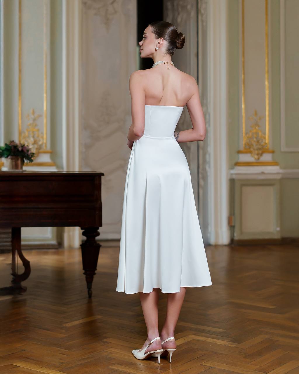 Woman in a white strapless dress standing in an elegant room with a piano.