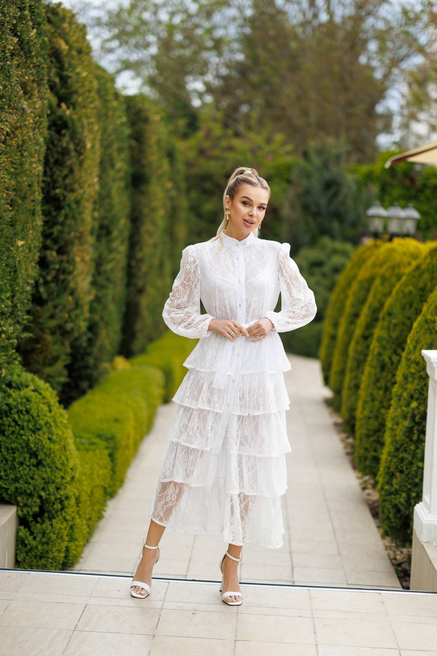 Woman in a white dress standing in a garden with manicured hedges.