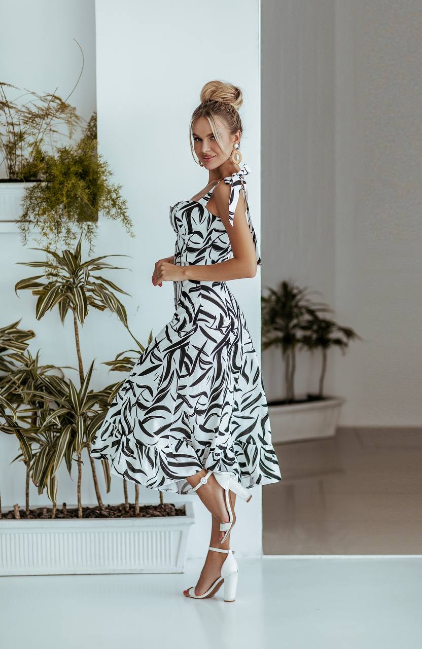 Woman in a black and white patterned dress standing in a room with plants.