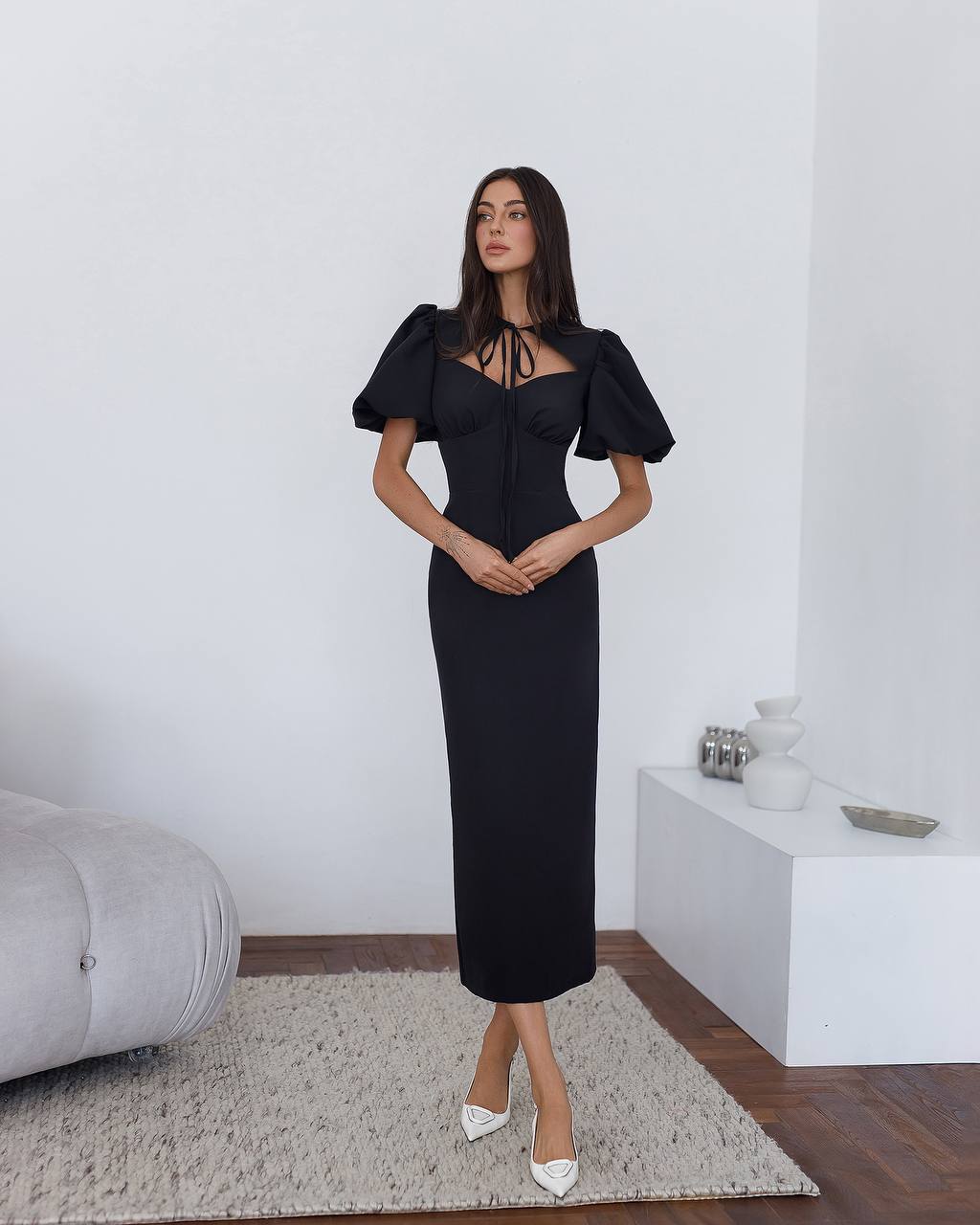 Woman wearing a black dress with puffed sleeves in a minimalistic room.