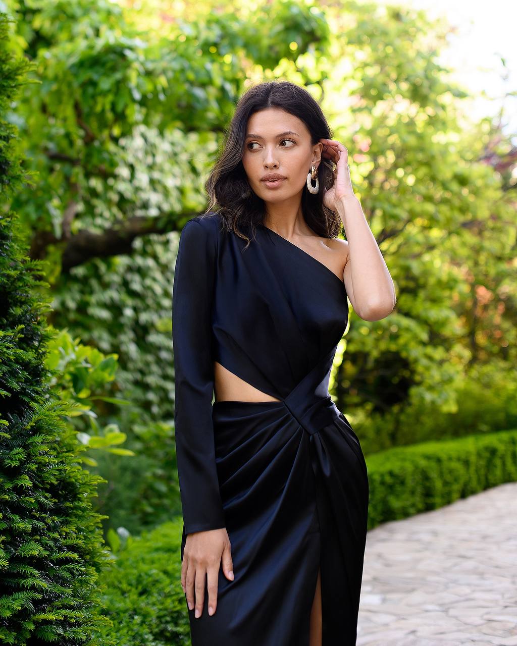 Woman in a black one-shoulder outfit standing in a garden