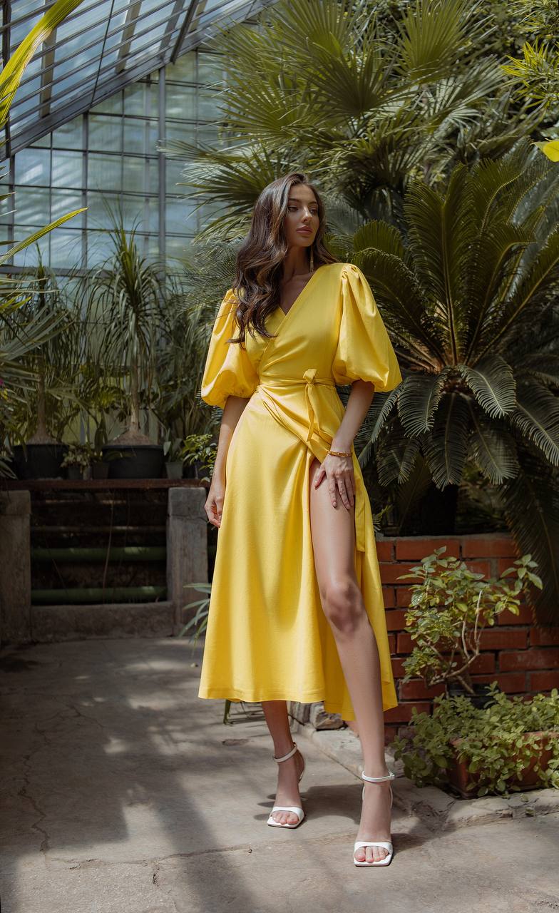 Woman in a yellow dress standing in a greenhouse with plants around