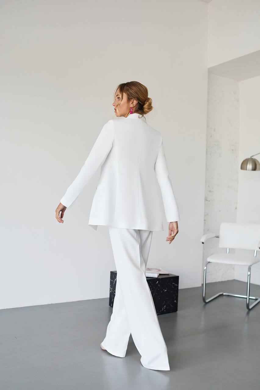 Person wearing a white suit in a minimalistic room with a chair and black box.