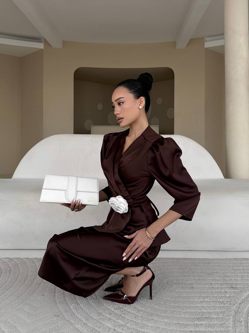 Woman in a brown dress holding a white box in an elegant interior setting