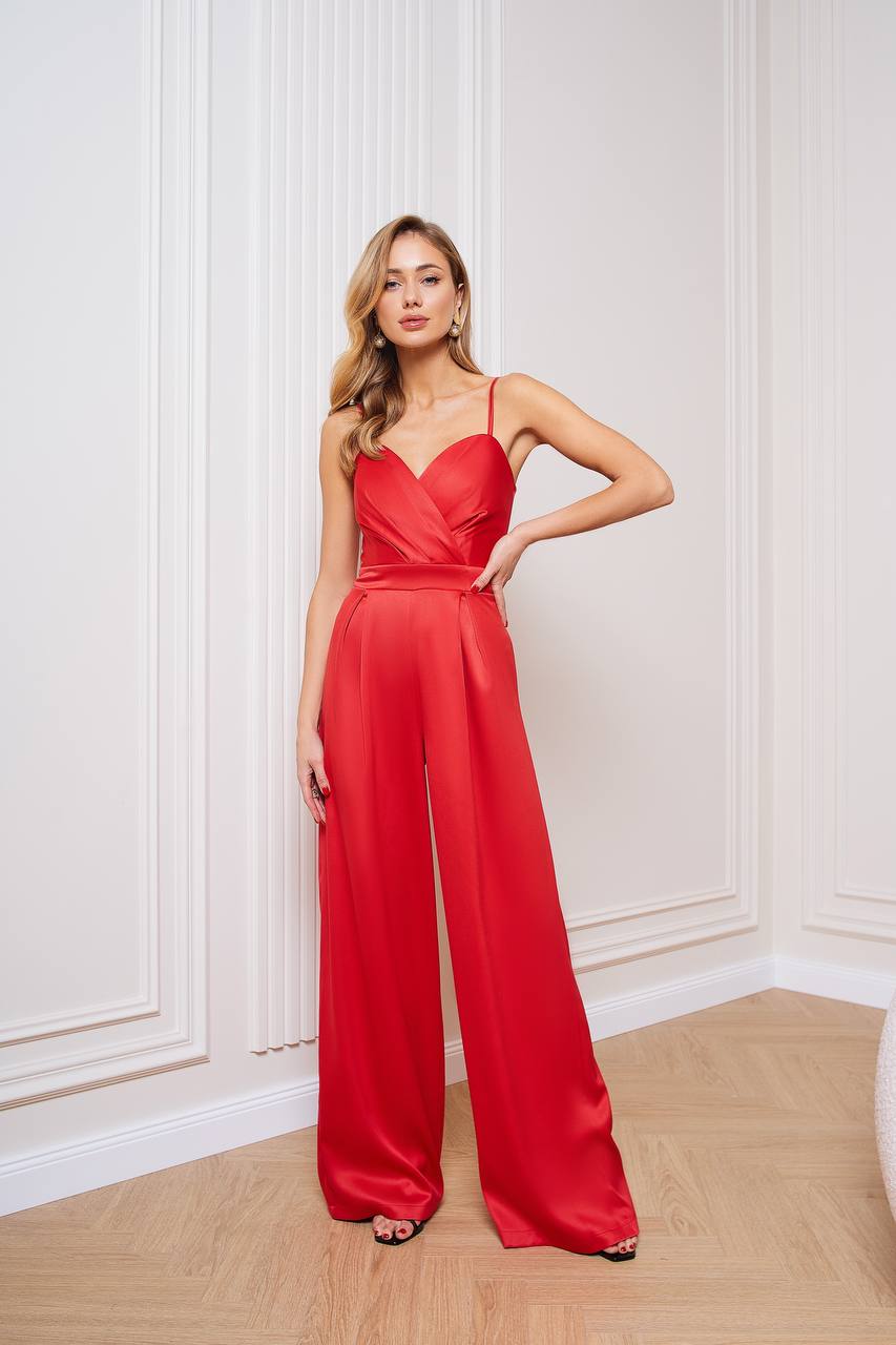 Woman wearing a red jumpsuit standing against a white wall.