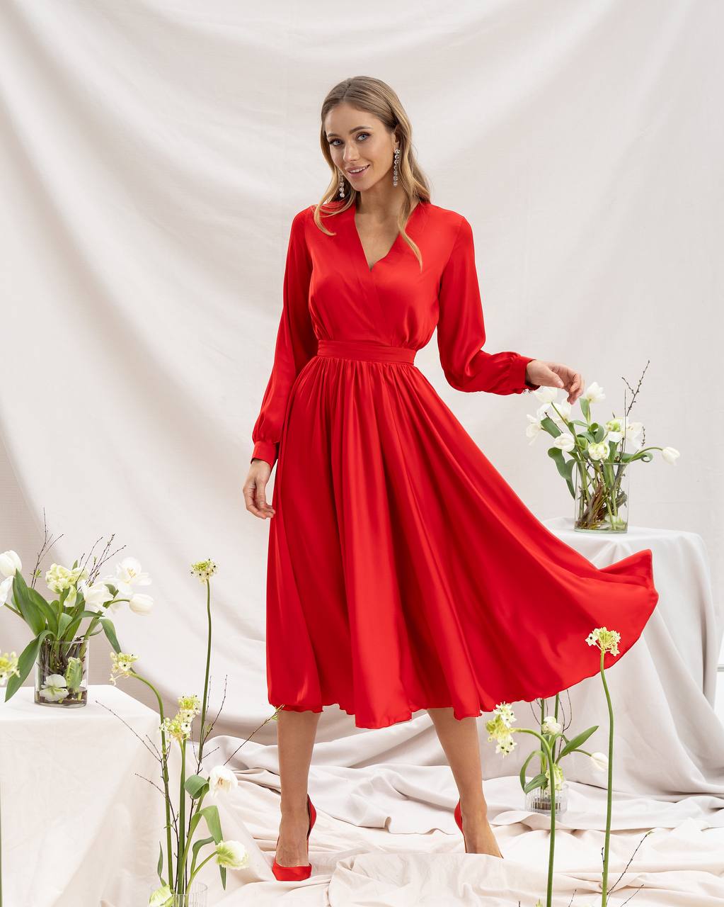 Woman wearing a red dress with long sleeves in a minimalistic setting.