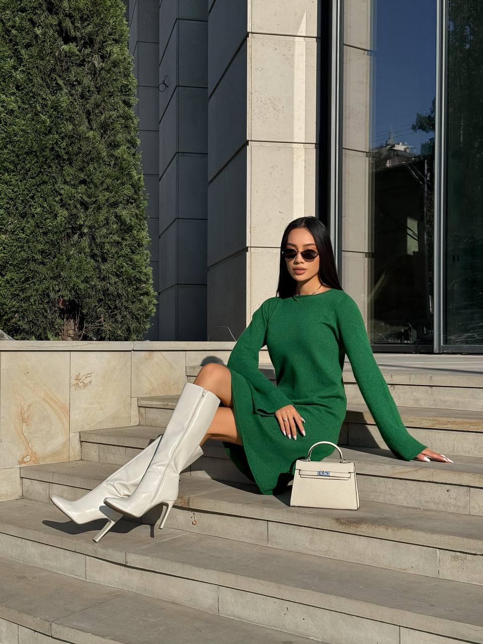 Woman in a green dress and white knee-high boots sitting on steps outdoors.