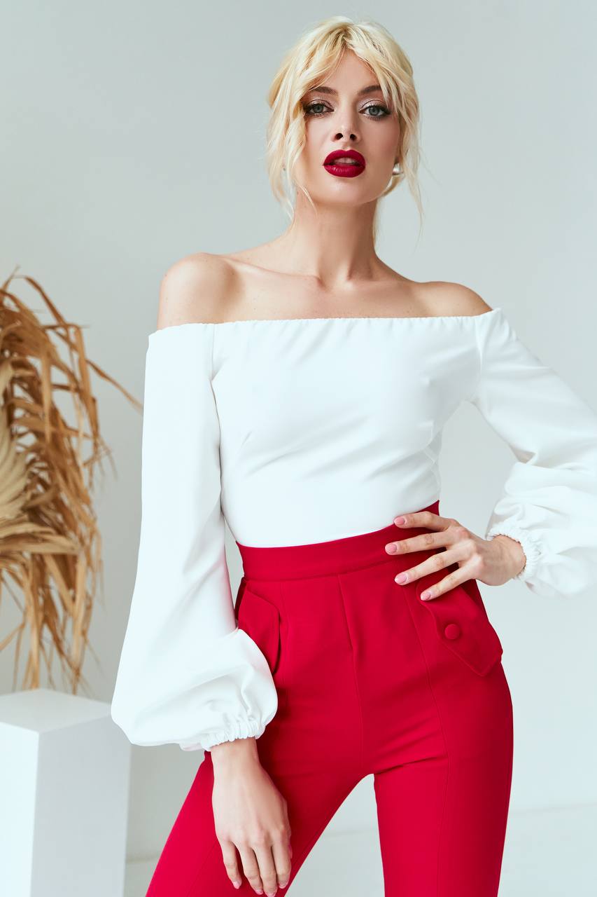 Woman wearing a white off-shoulder top and red pants against a plain background