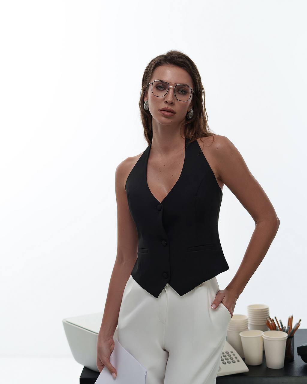 Woman wearing a black sleeveless top and white pants in an office setting