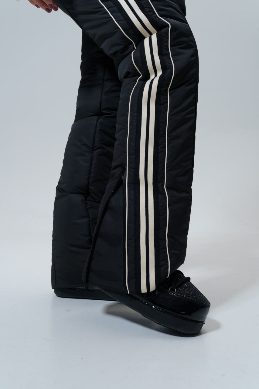 Black puffer pants with white stripes worn by a person on a light gray background