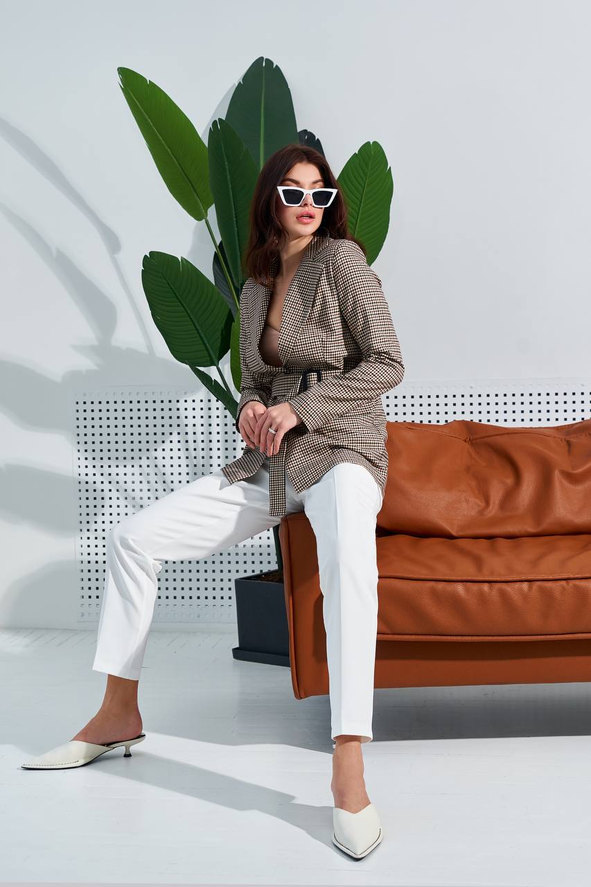 Woman in stylish outfit sitting on a brown couch with a plant in the background
