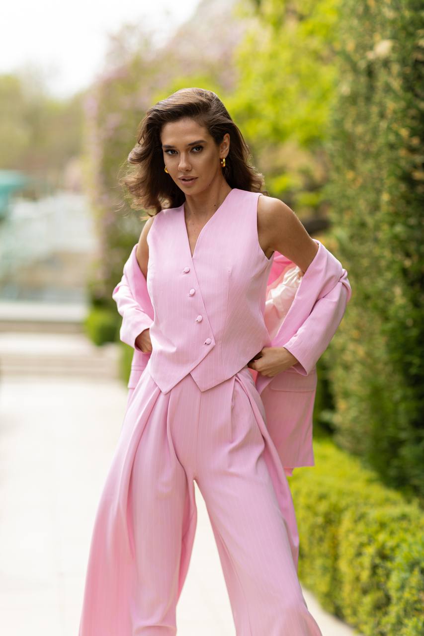 Woman wearing a pink suit standing outdoors with greenery in the background