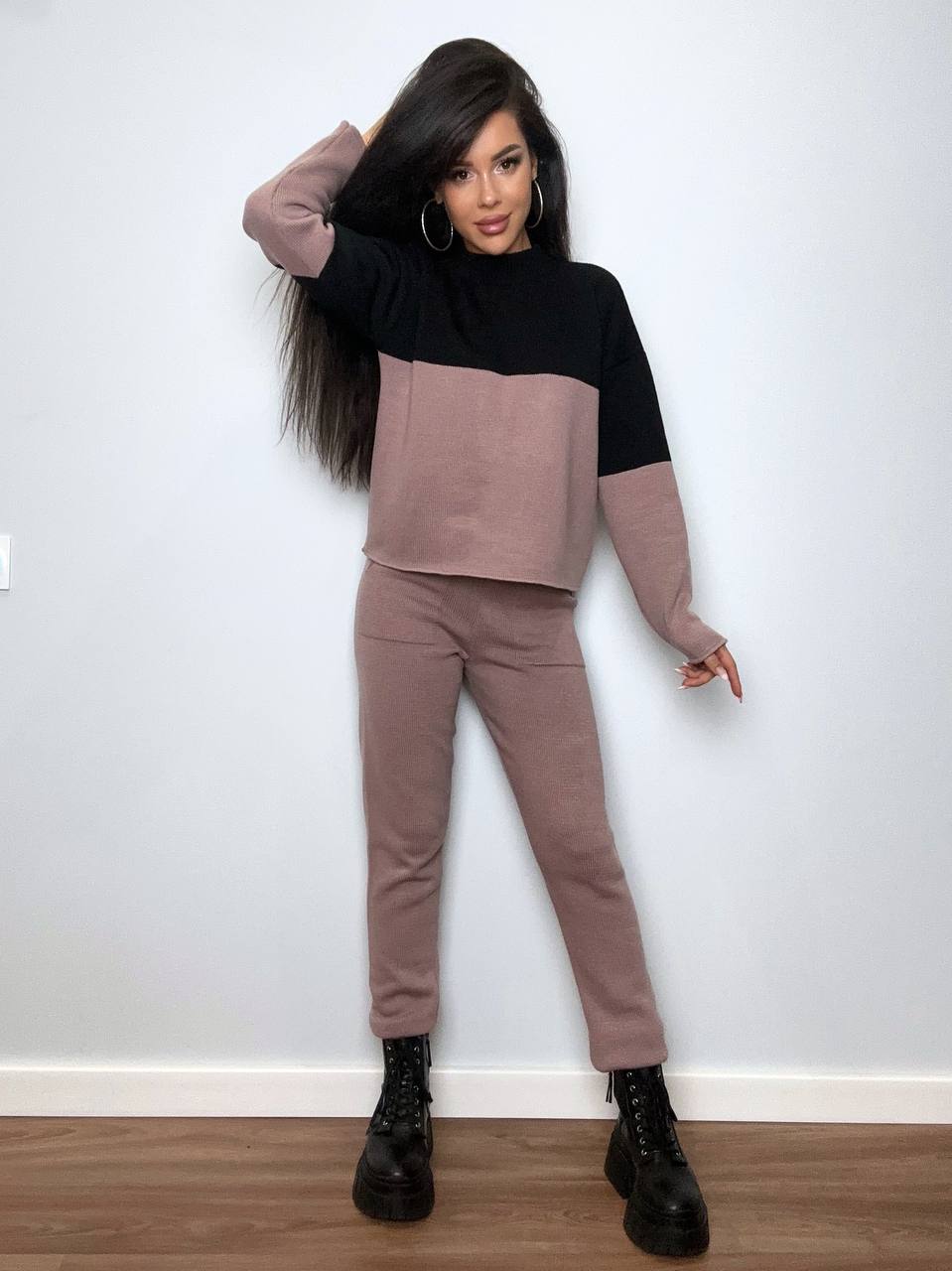 Woman wearing a two-tone outfit with a black and beige top and pants against a white wall.