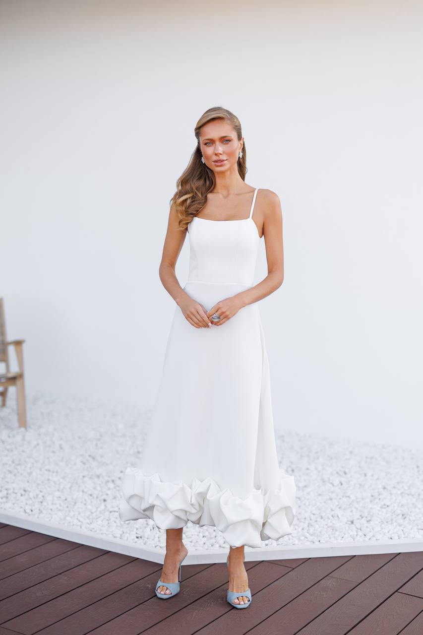 Woman in a white dress standing on a wooden deck with a white wall background