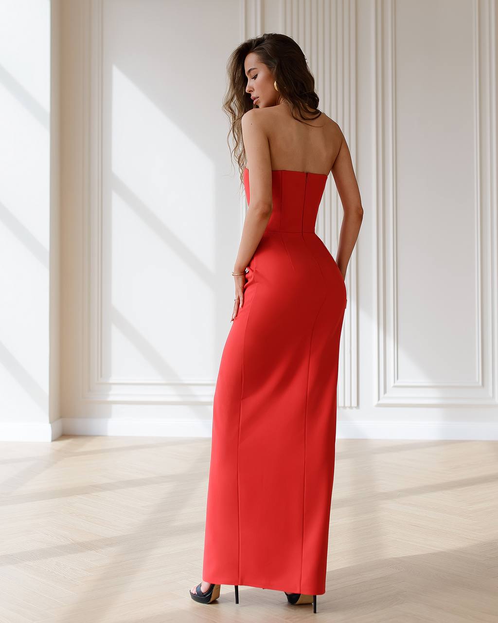 Woman wearing a red strapless gown in a bright room with white walls.