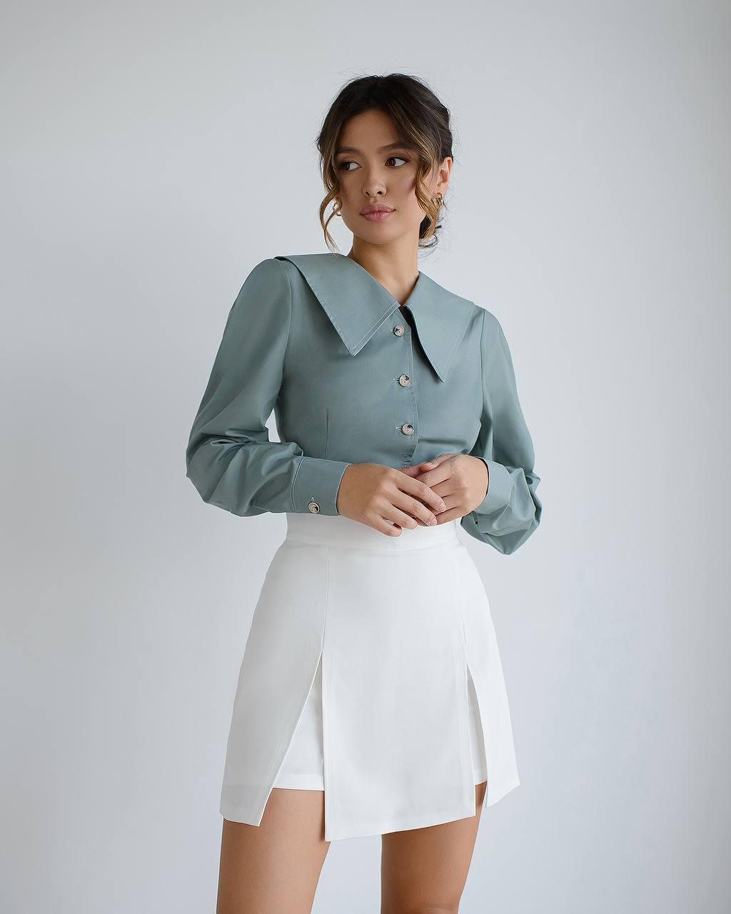 Woman wearing a light blue shirt and white skirt against a plain background