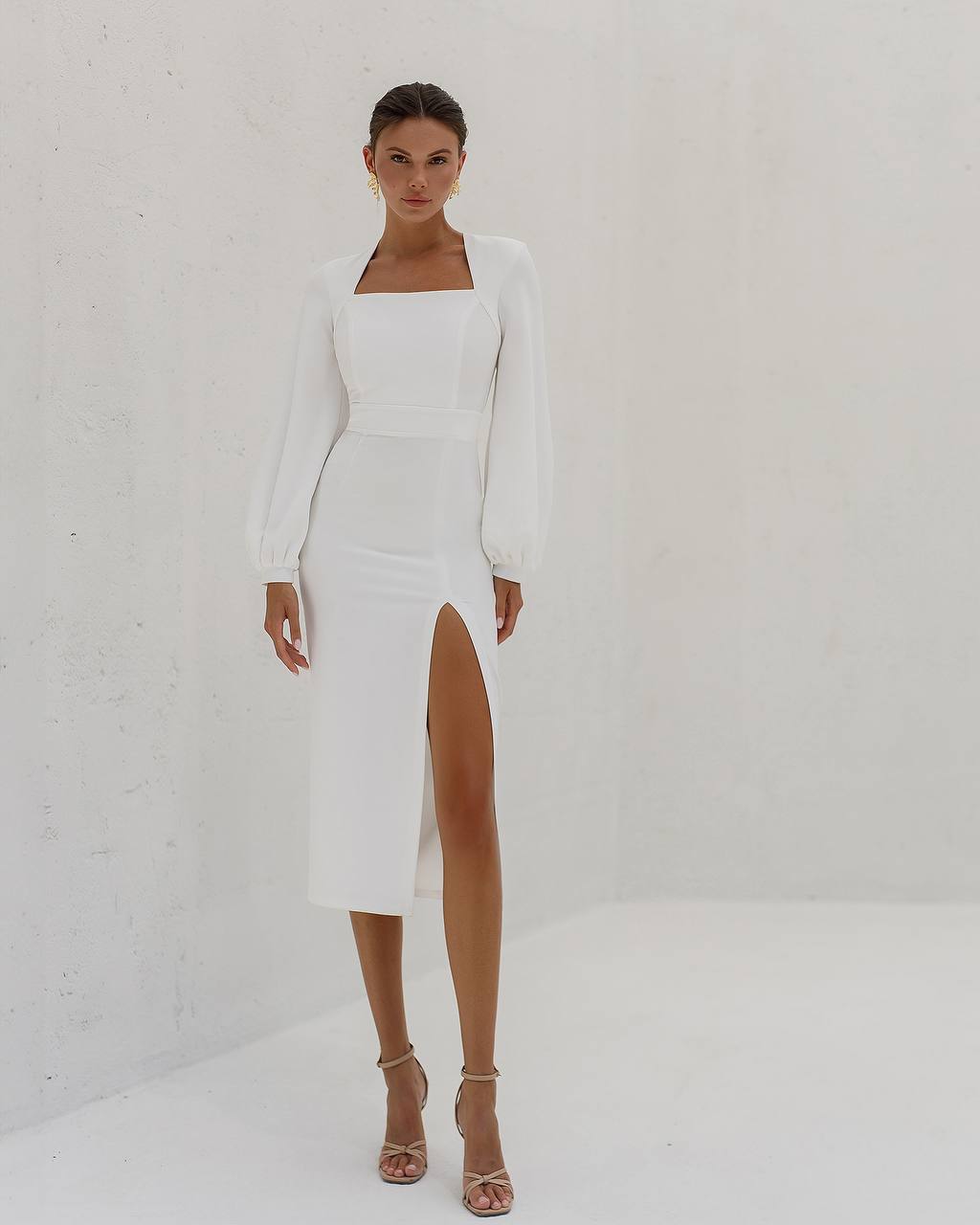 Woman wearing a white dress with a slit on a plain background