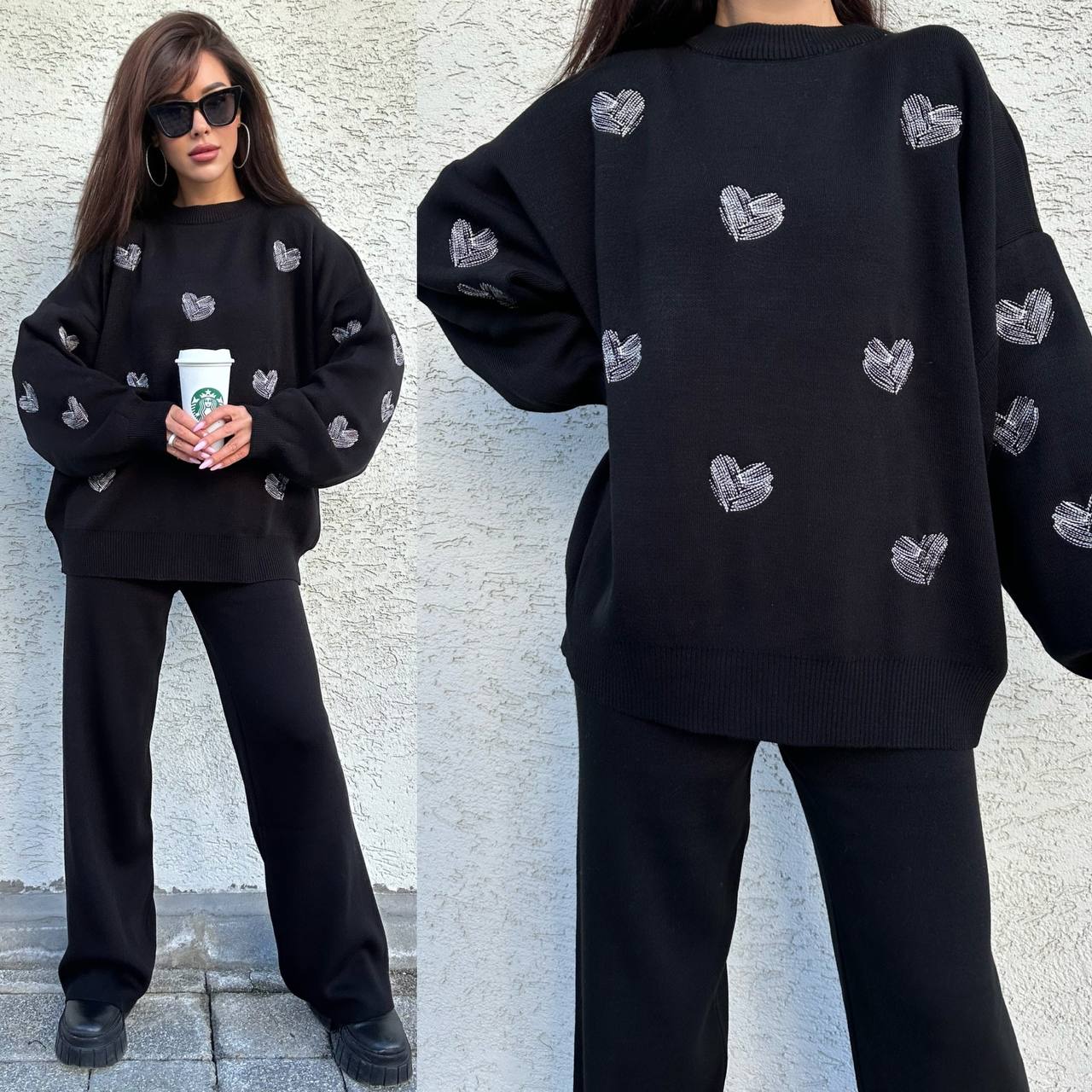 Person wearing a black sweater with heart patterns, holding a Starbucks cup, against a light gray wall.