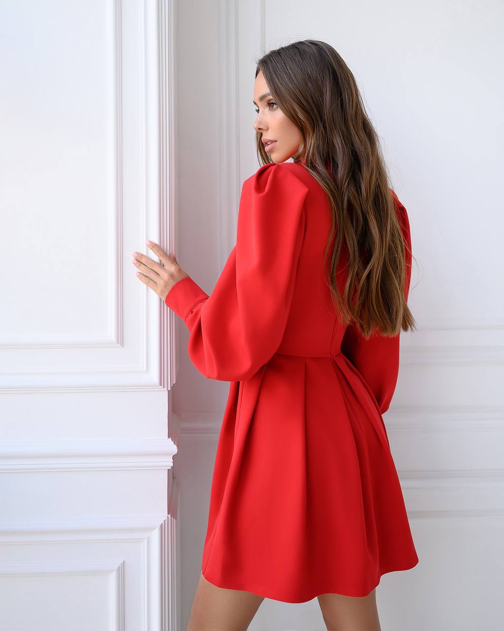 Woman wearing a red dress standing against a white wall.