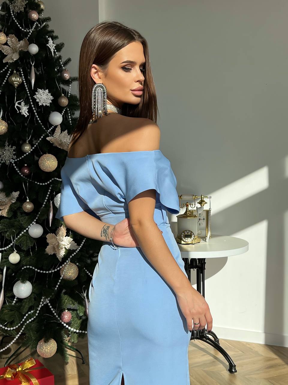 Woman in a blue off-shoulder dress standing next to a decorated Christmas tree.