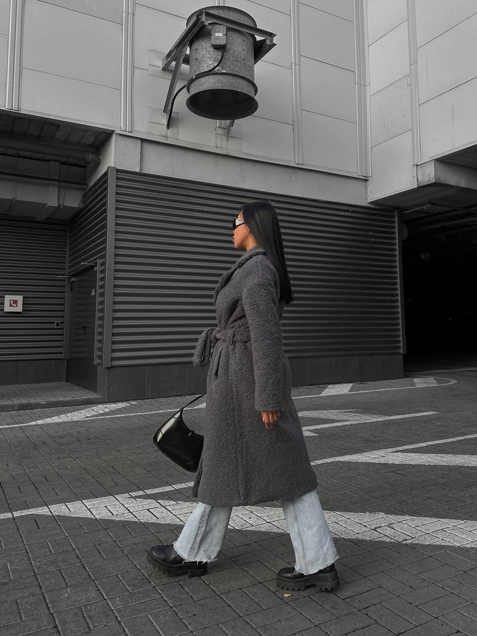 Person wearing a long coat walking on a street with a building in the background