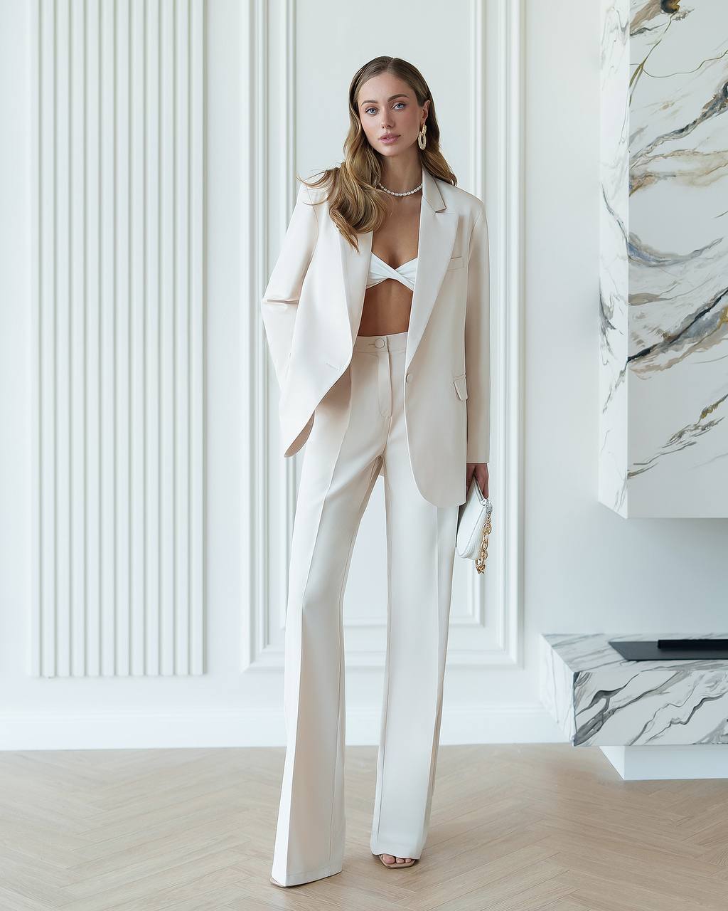 Woman in a stylish outfit with a white blazer and pants in a modern interior setting.
