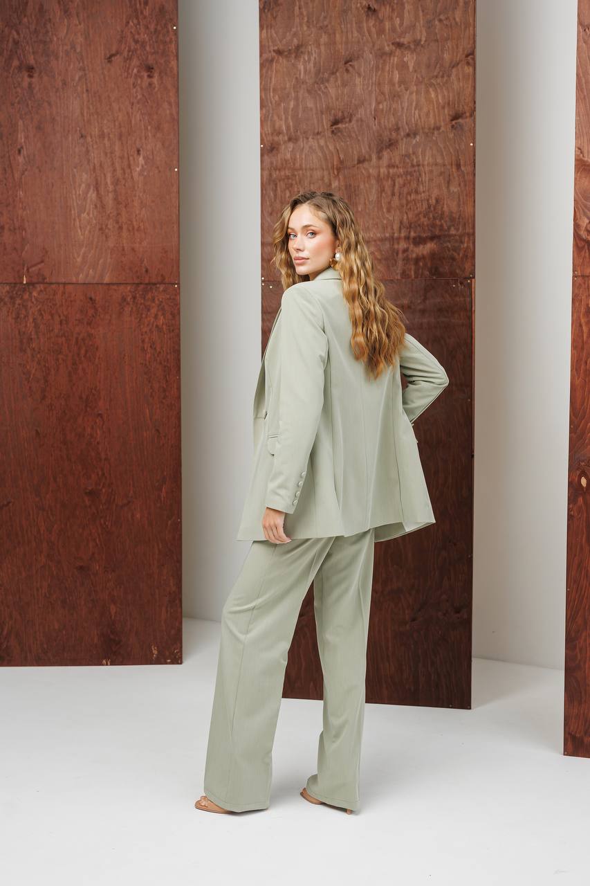 Woman in a light green suit standing against a wooden wall.