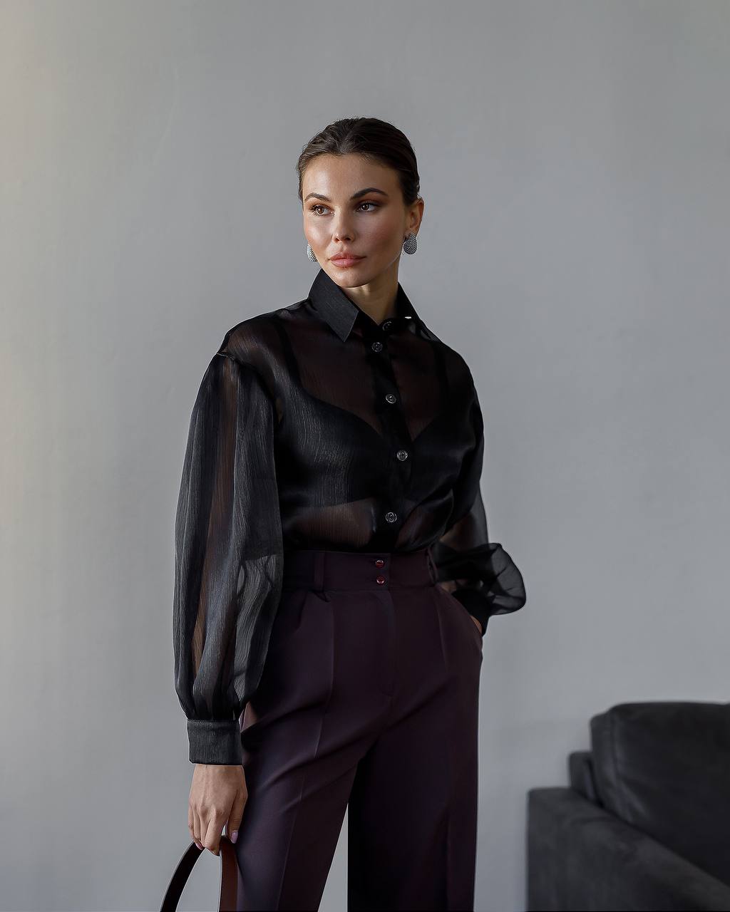Woman wearing a black blouse and dark pants against a gray background