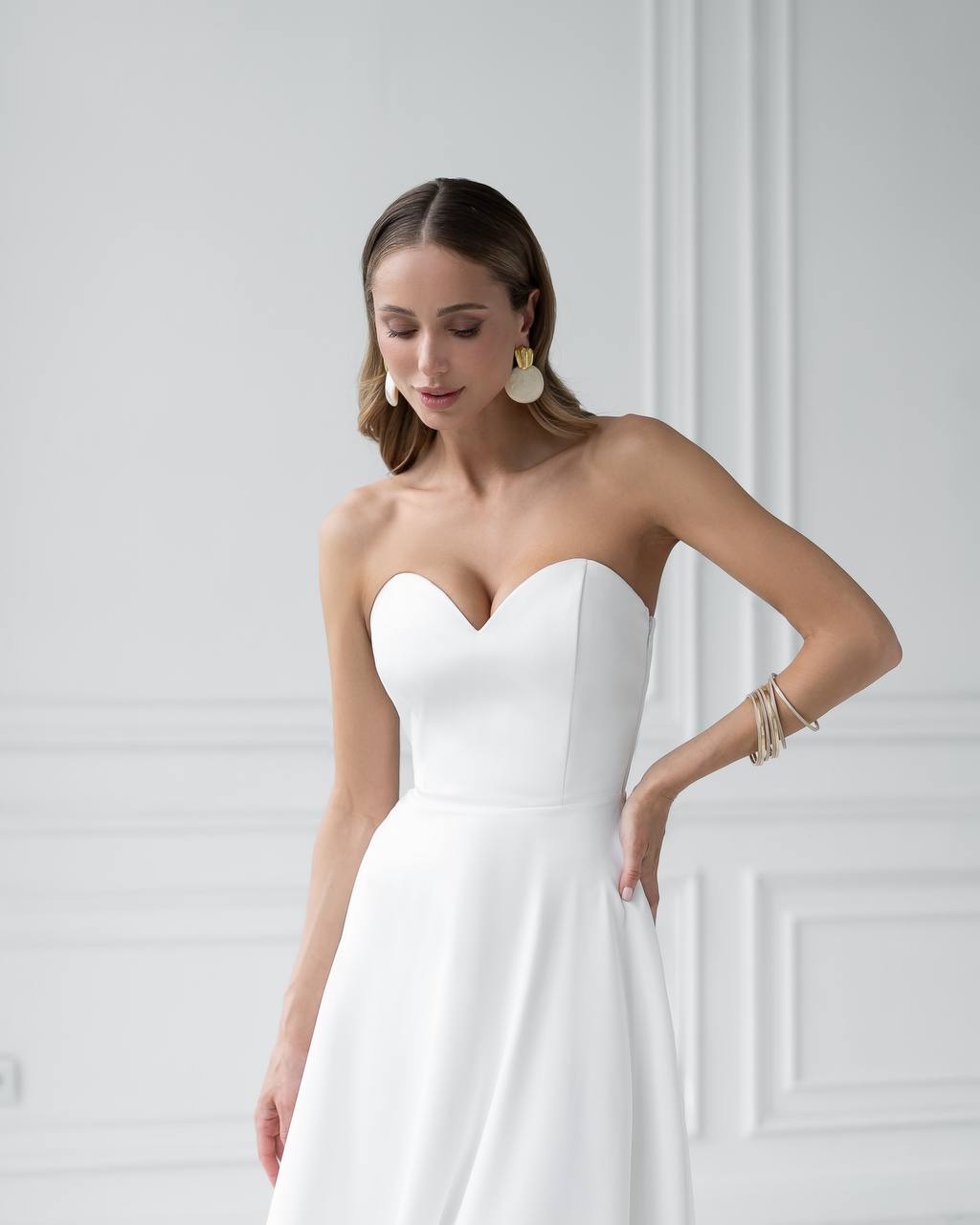 Woman wearing a strapless white wedding dress against a white wall