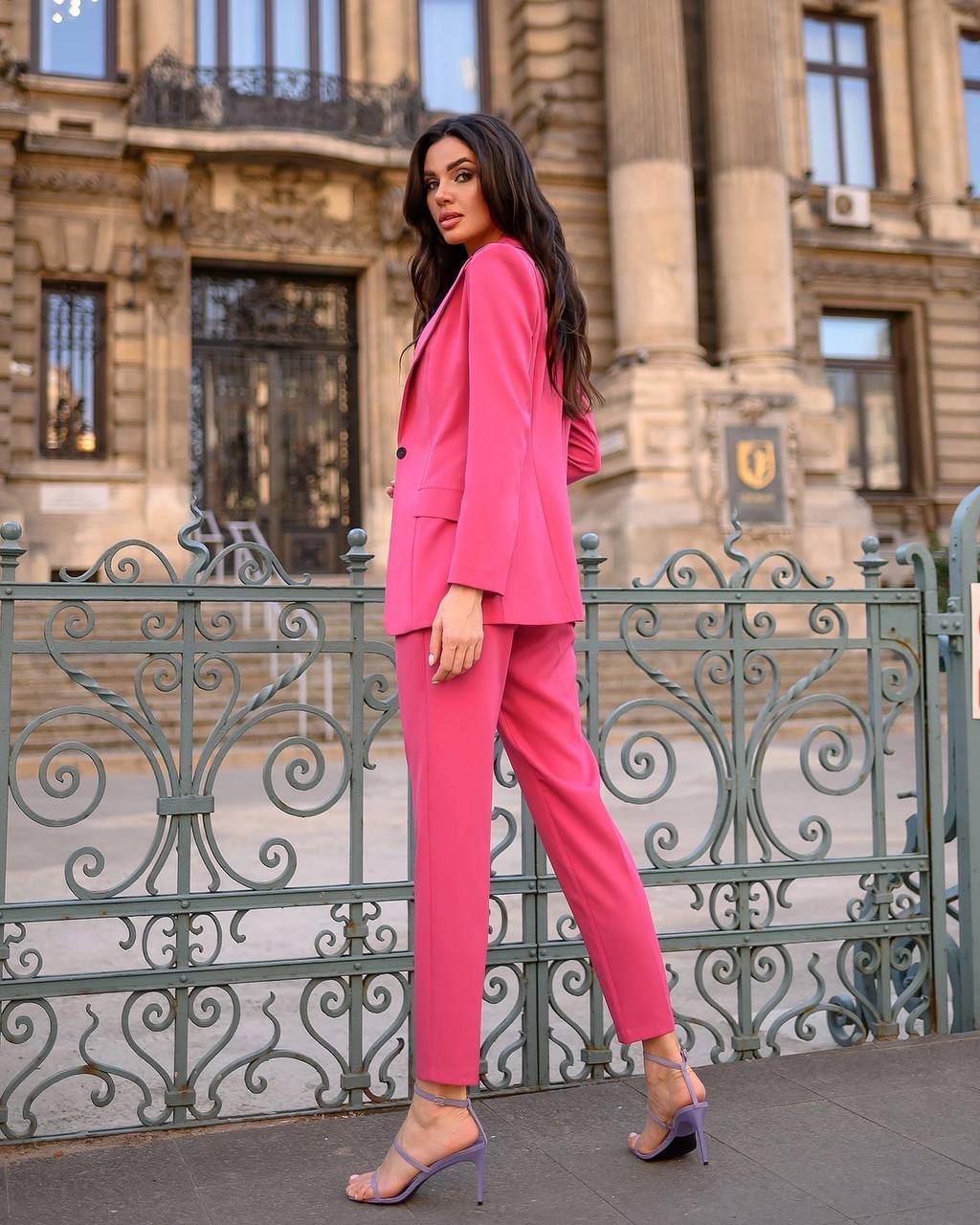 Woman in a pink suit standing in front of an ornate building.