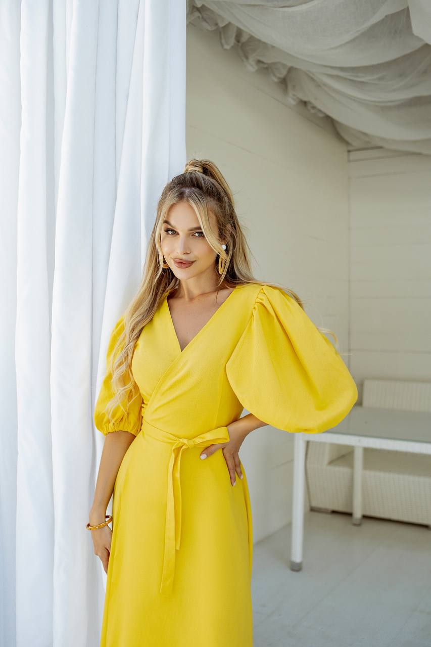 Woman wearing a yellow dress with puffed sleeves in a bright room.