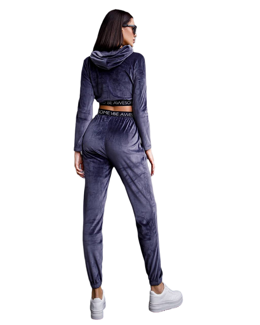 Woman wearing a gray velour tracksuit with white sneakers on a white background