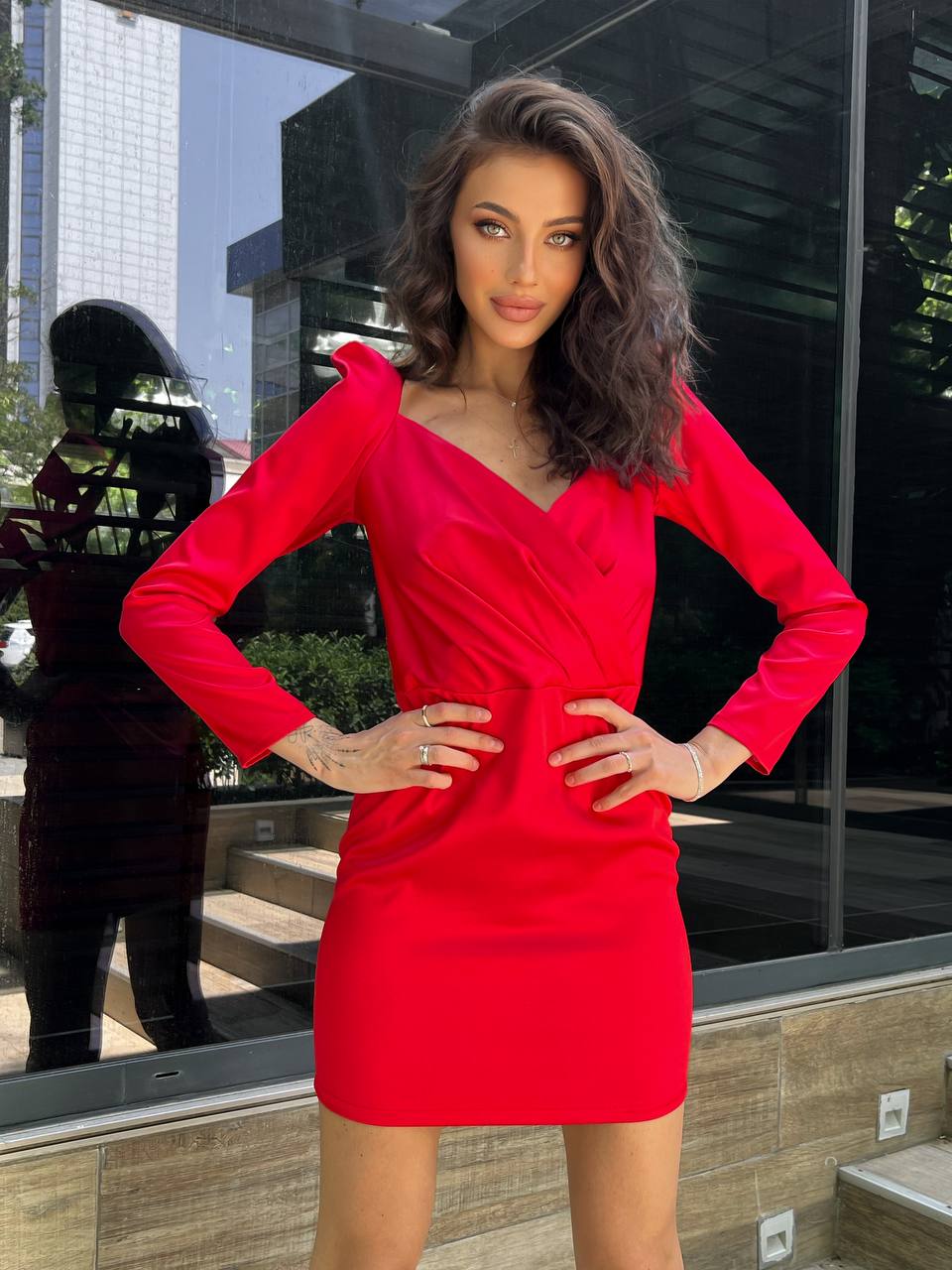 Woman in a red dress standing in front of a reflective glass surface with cityscape background
