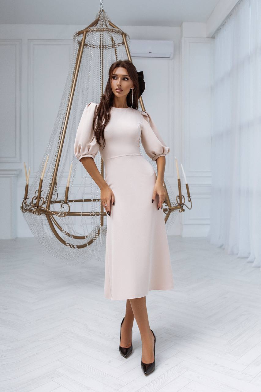 Woman in a light pink dress standing in a white room with decorative elements.