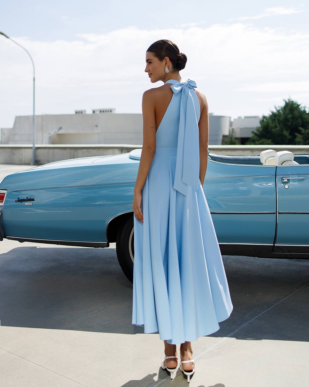 Woman in a light blue dress standing next to a vintage car
