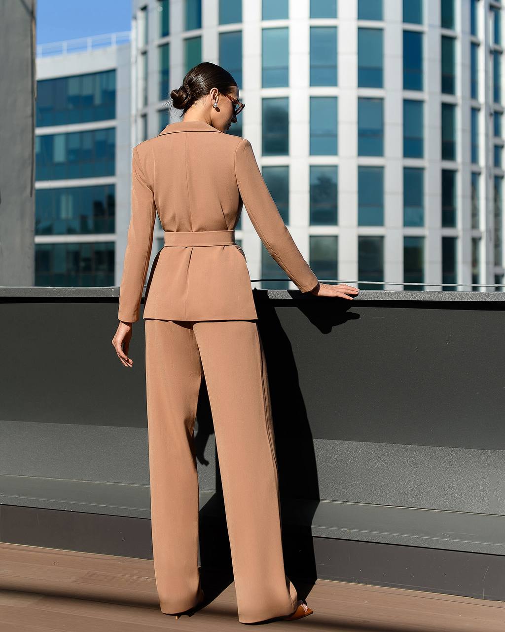 Woman in a beige suit standing on a rooftop with modern buildings in the background