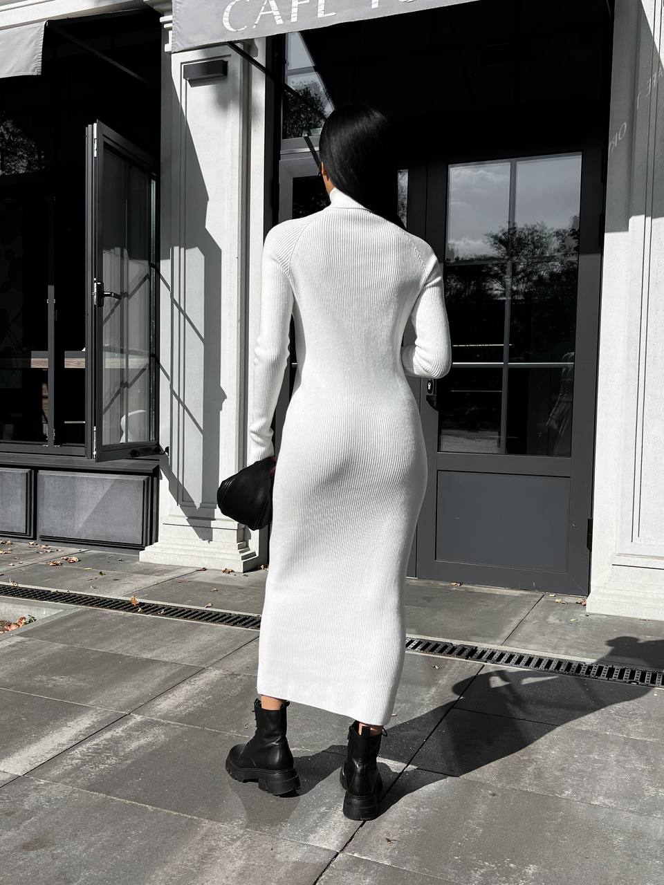 Person wearing a white dress with a high slit standing on a sidewalk in front of a building.