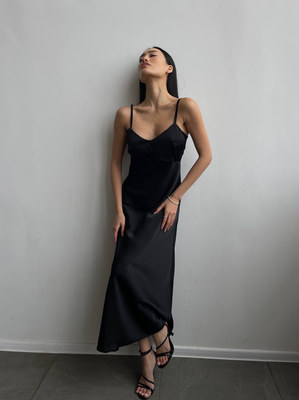 Woman wearing a black slip dress against a plain wall