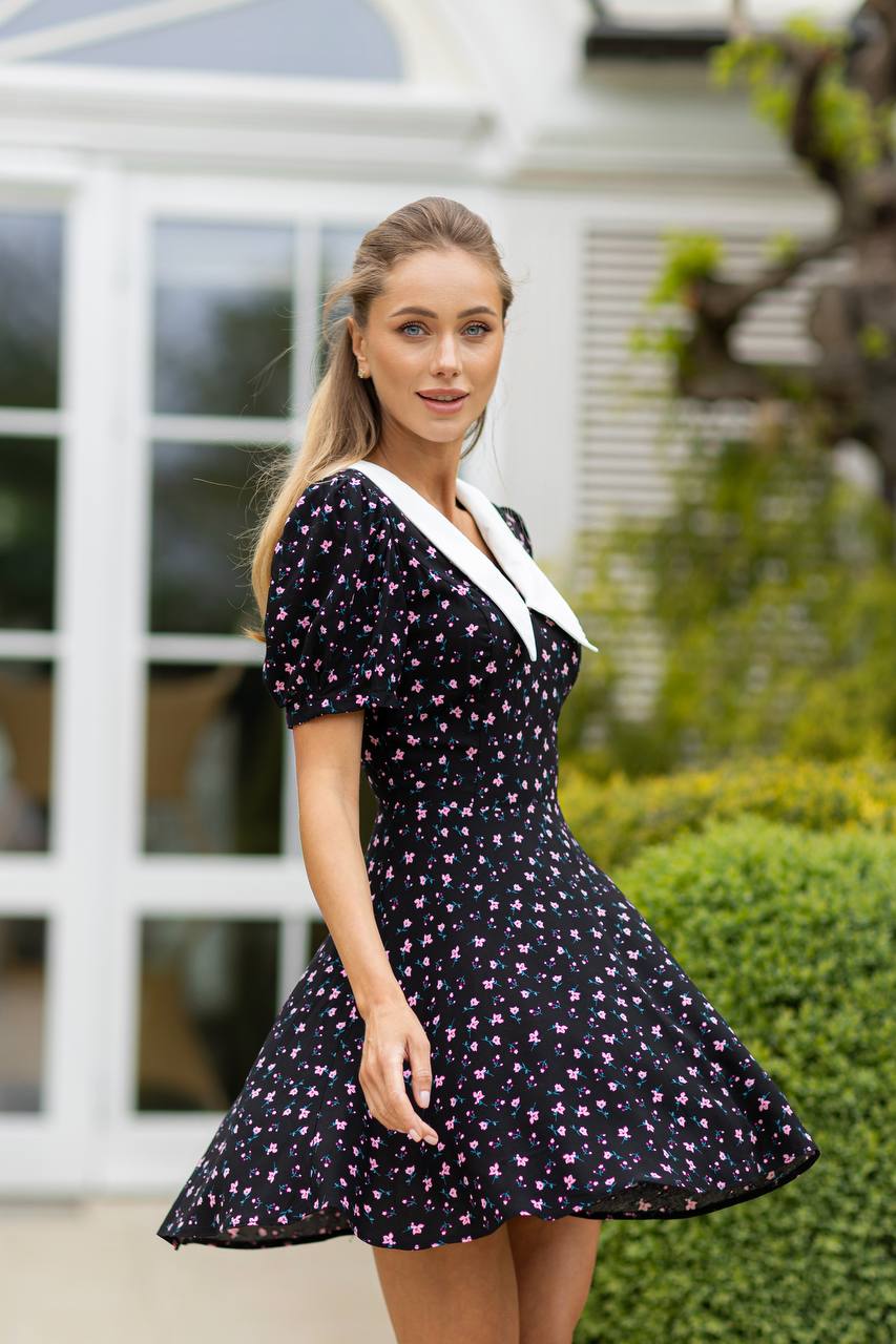 Woman wearing a black floral dress with a white collar outdoors.