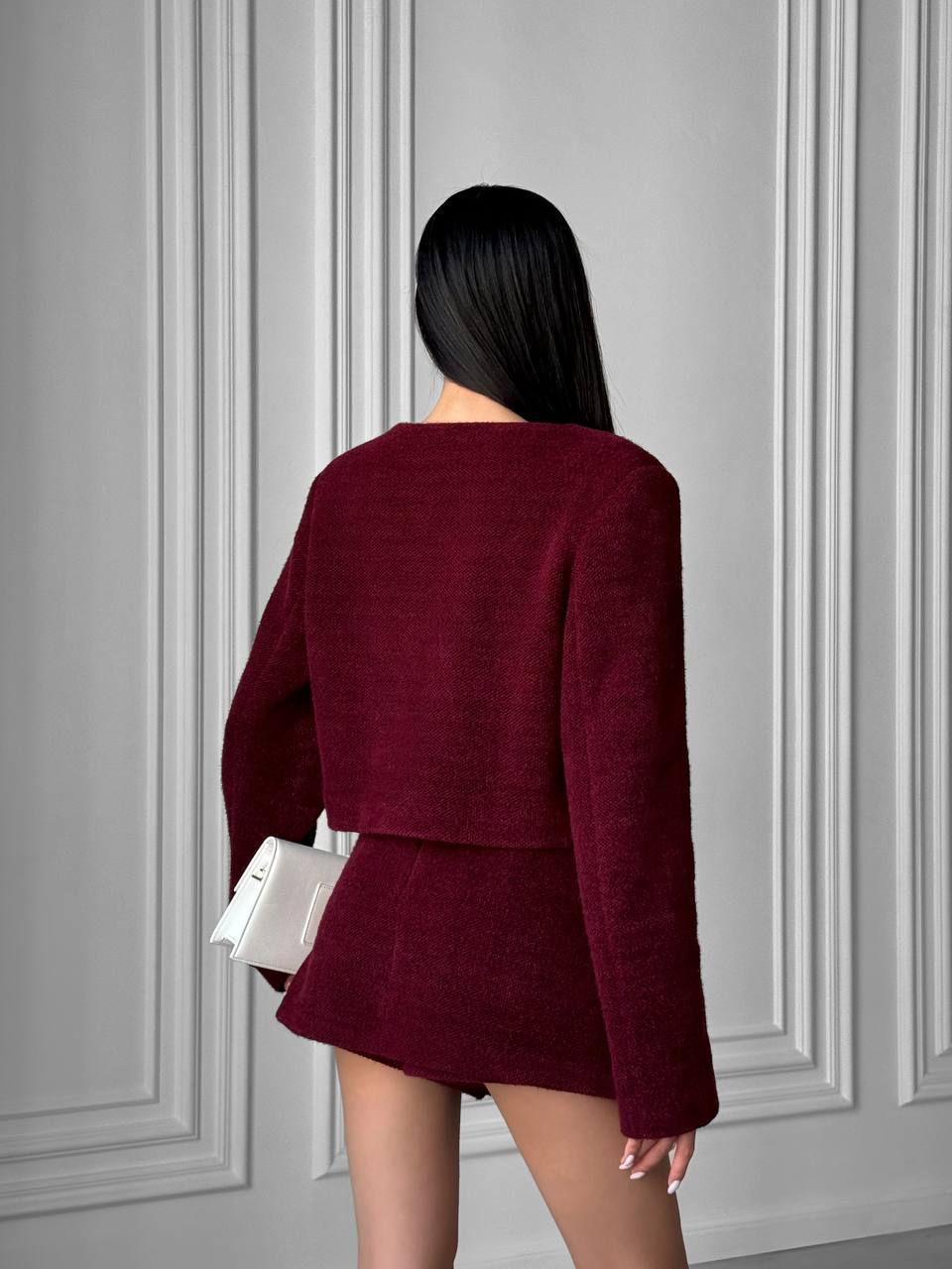 Person wearing a burgundy outfit against a gray paneled wall