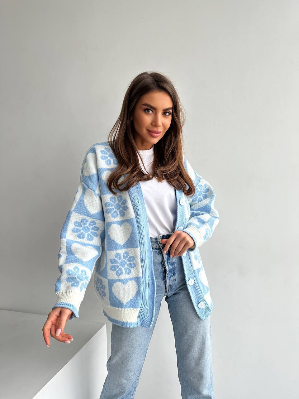 Woman wearing a light blue cardigan with heart patterns on a plain background