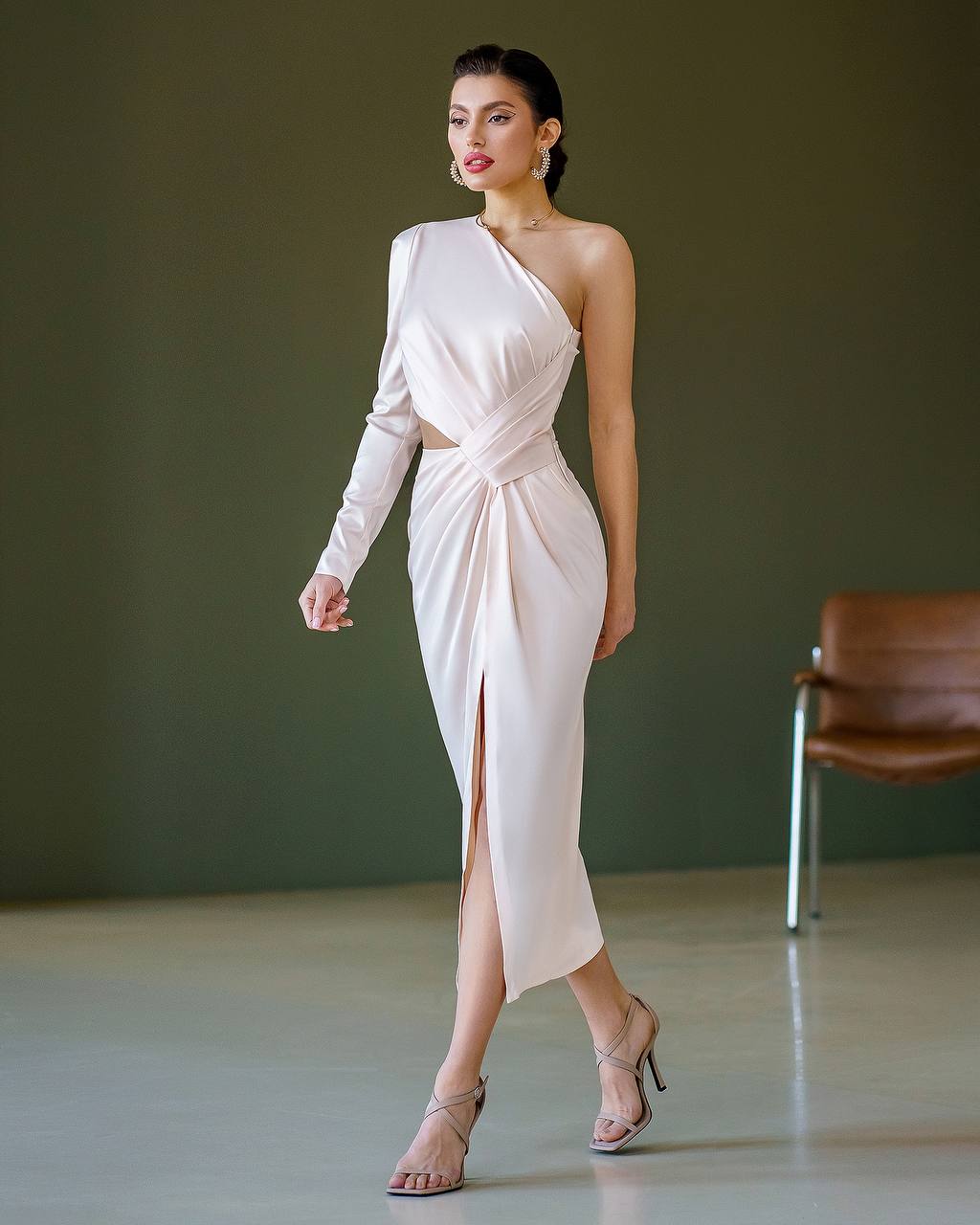 Woman wearing a white one-shoulder dress with a slit, standing against a plain background.