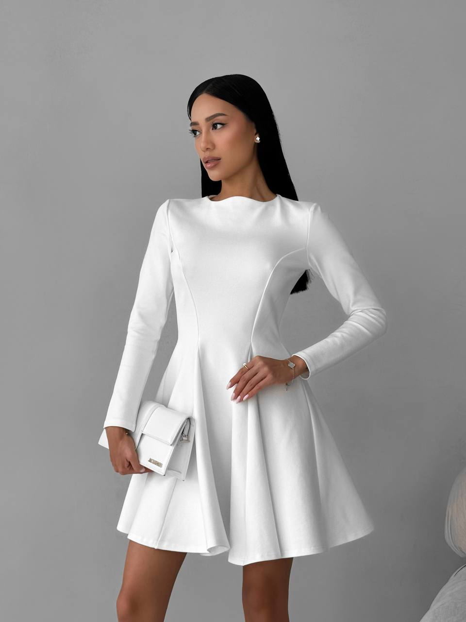 Woman wearing a white dress with long sleeves against a gray background