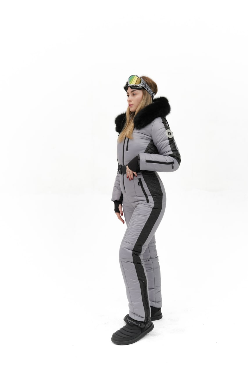 Person wearing a gray and black ski suit with fur-lined hood on a white background