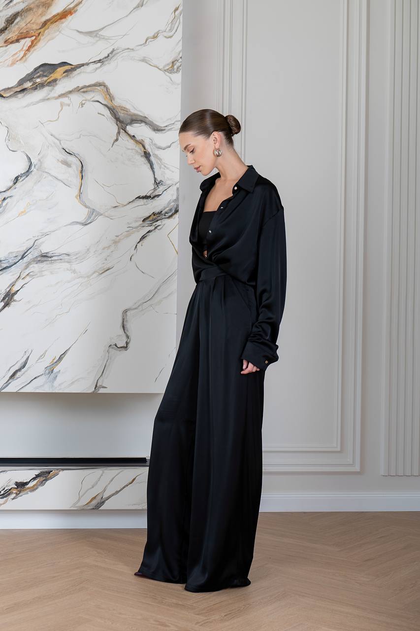 Woman in a black dress standing in a room with marble wall and wooden floor.