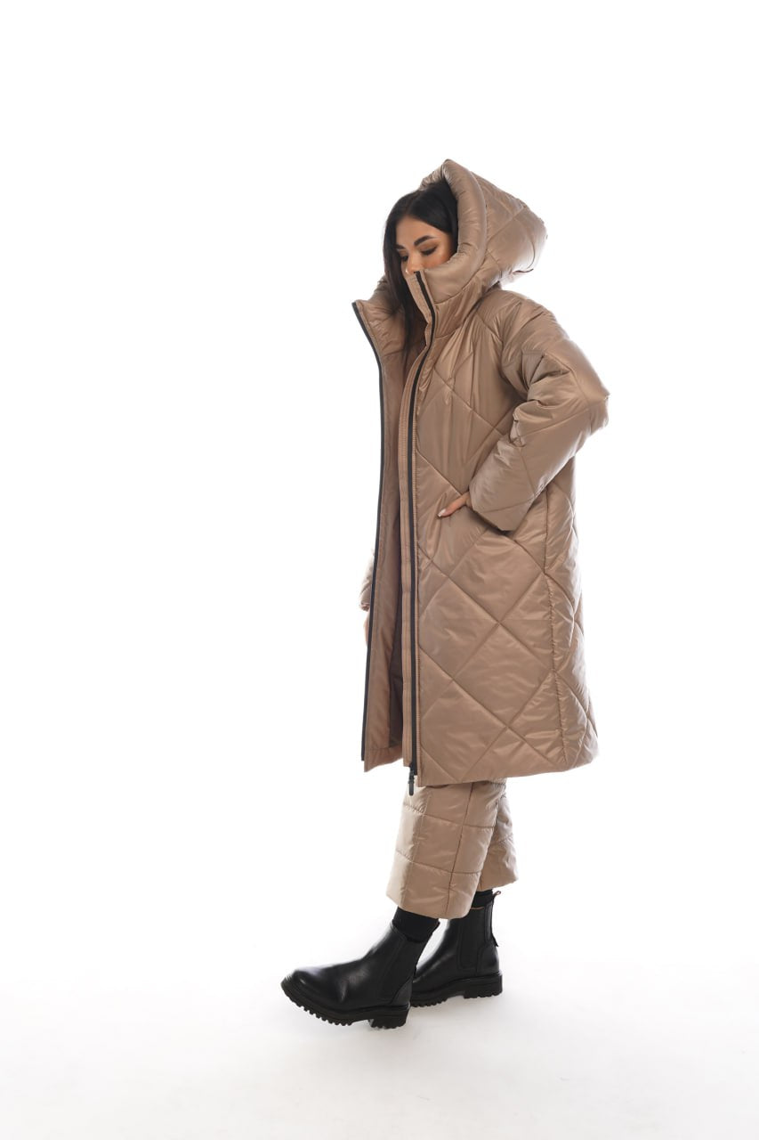 Person wearing a long quilted beige coat with a hood on a white background