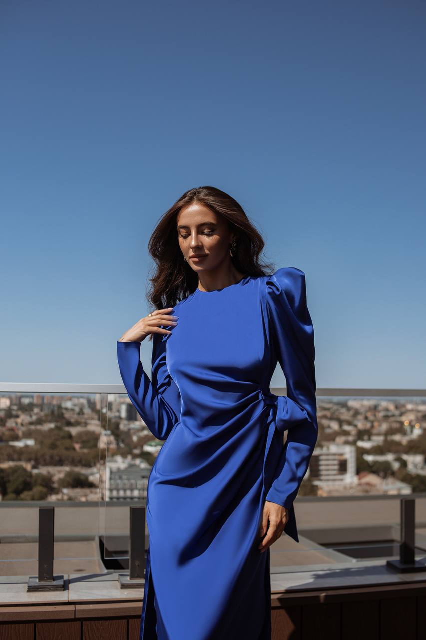Woman in a blue dress standing on a rooftop with a cityscape in the background