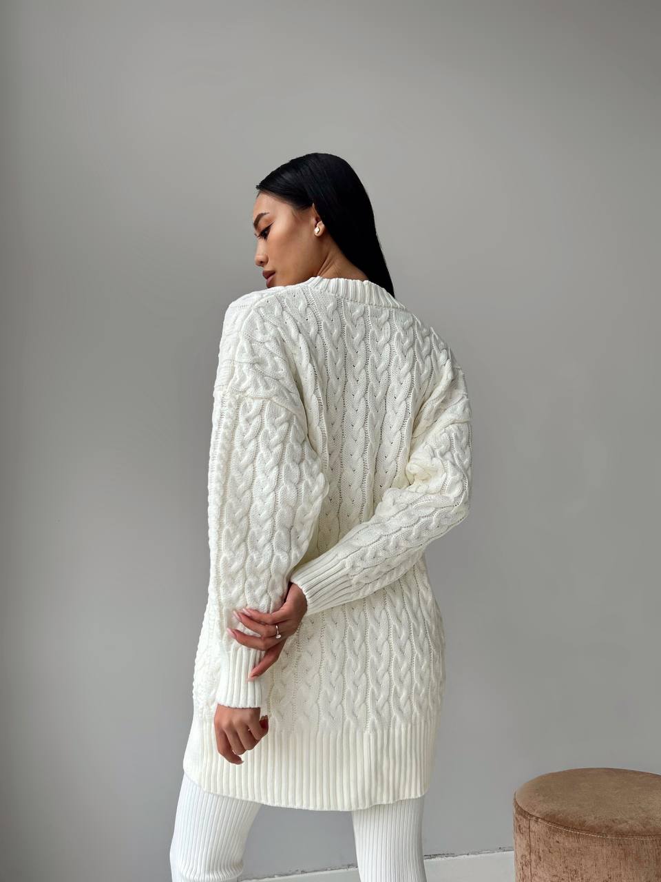 Woman wearing a white cable knit sweater against a plain background
